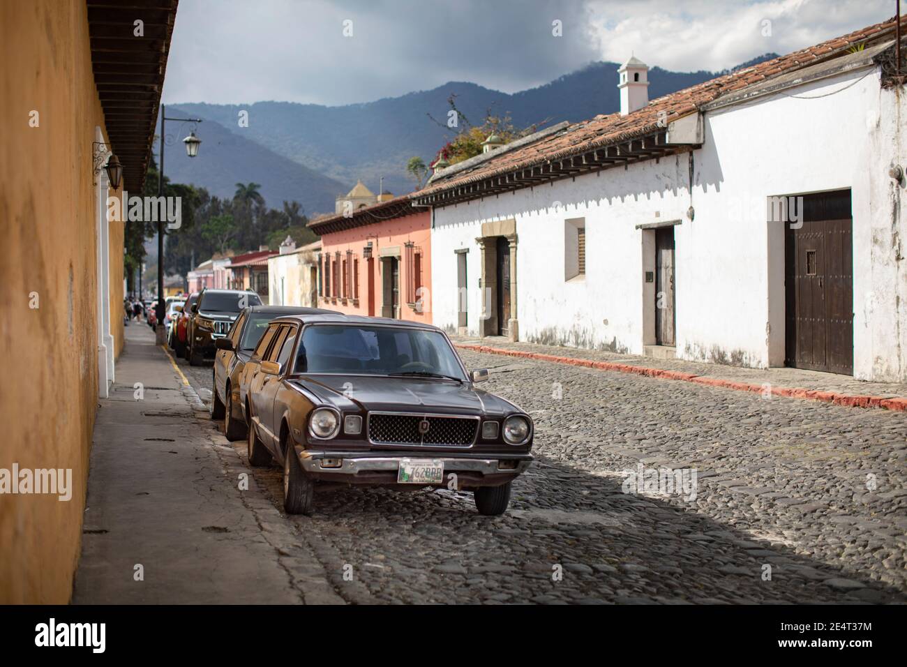 Un'auto d'epoca è parcheggiata lungo una strada acciottolata ad Antigua, Guatemala, America Centrale Foto Stock