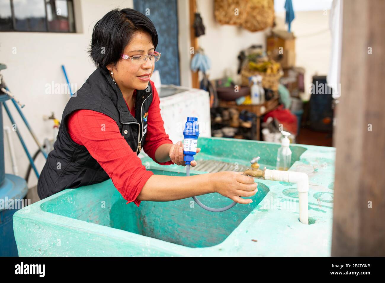 Una donna utilizza un sistema di filtrazione dell'acqua pulita basato sul rubinetto a casa sua a Cantel, Guatemala. Foto Stock
