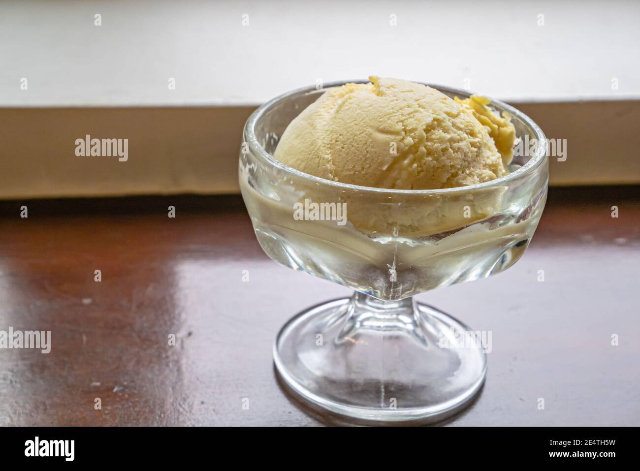 Il primo piano di un gustoso gelato alla vaniglia fresco fatto in casa scoop in tazza di vetro su sfondo tavola di legno vintage Foto Stock