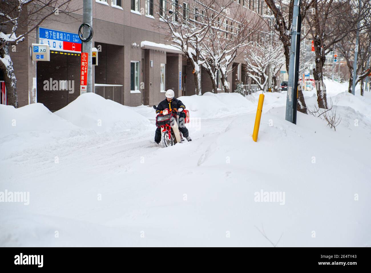 Un postino giapponese su una moto che attraversa una strada innevata. Foto Stock