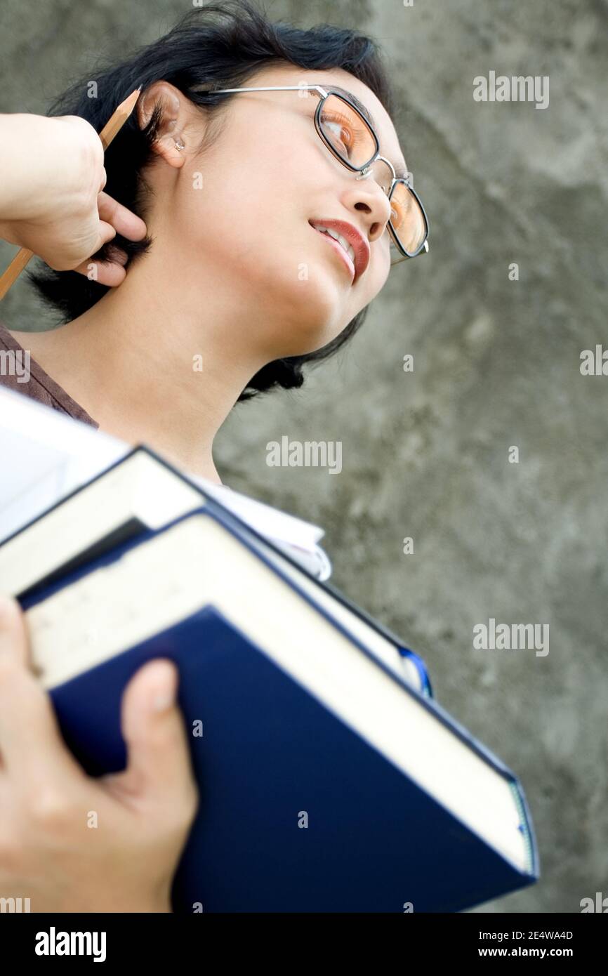 astuto che osserva la donna asiatica di affari che tiene la pila di letteratura e. una matita su uno sfondo scuro della parete guardando entusiasta per il prossimo evento Foto Stock