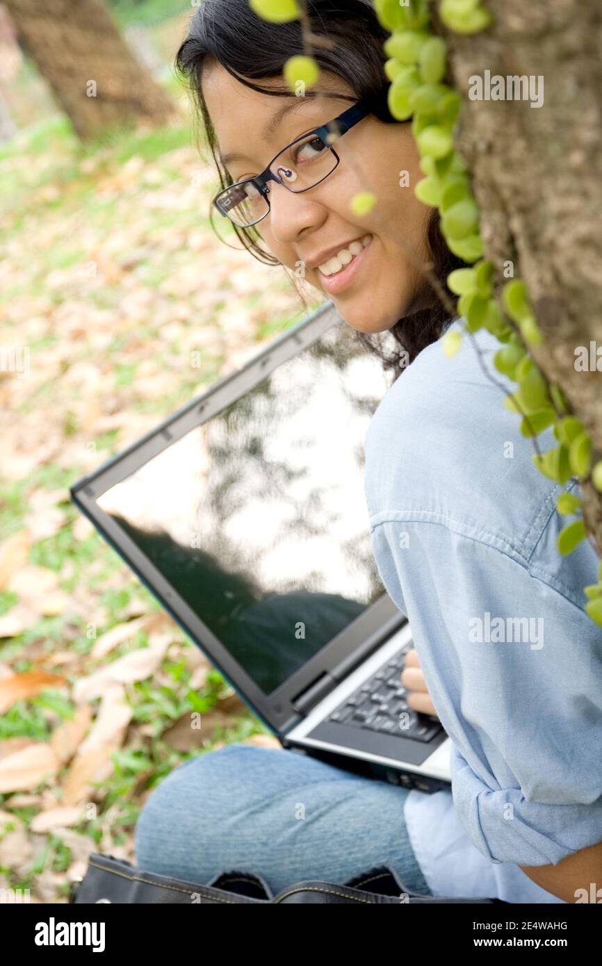 ritratto di bella studentessa di università femminile asiatica che lavora su un laptop sotto un albero Foto Stock