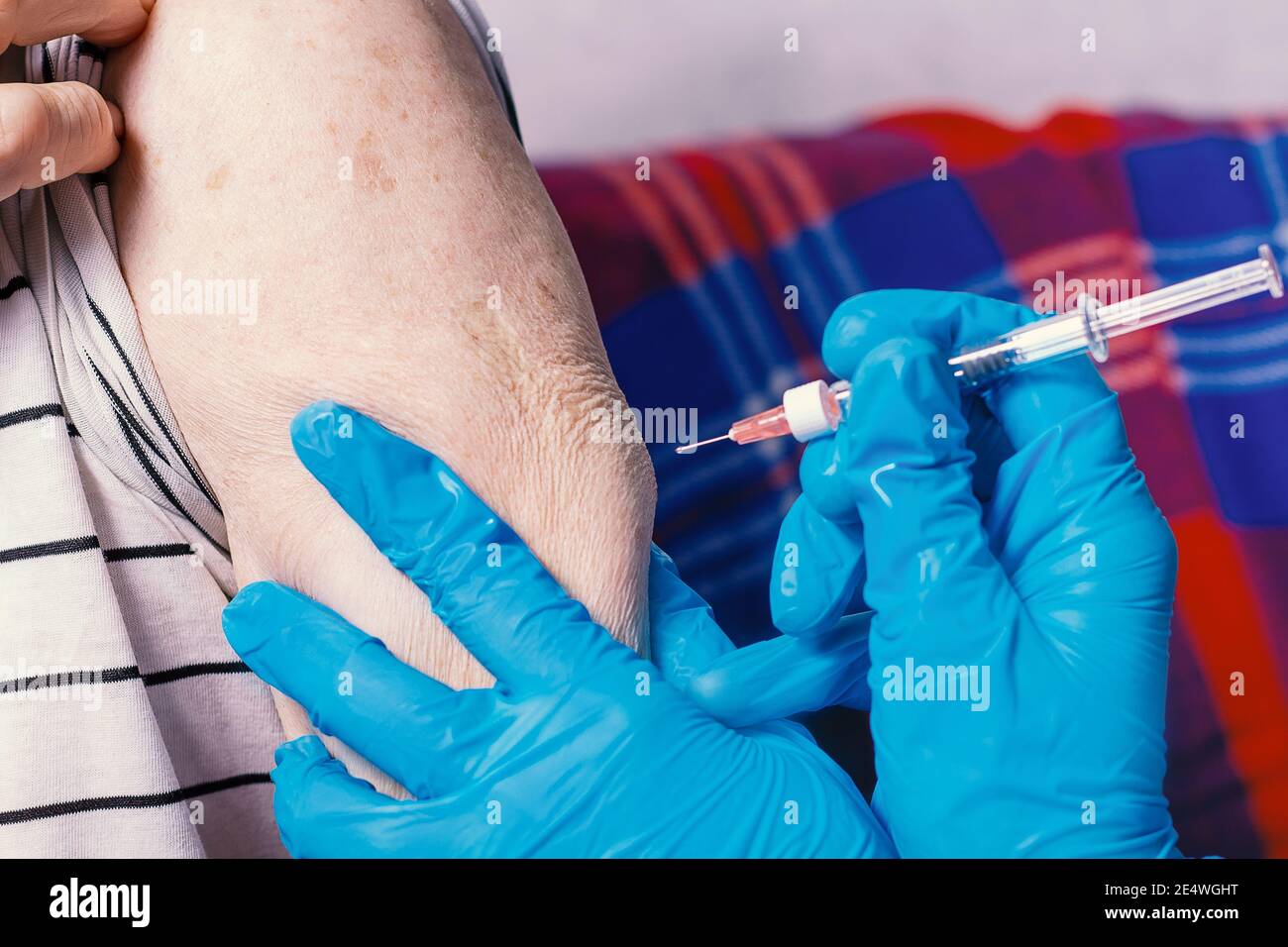 L'uomo molto anziano sta ricevendo il vaccino del coronavirus. Primo piano. Iniezione a persone anziane a casa. Siringa con medici mani in guanti blu. Foto Stock