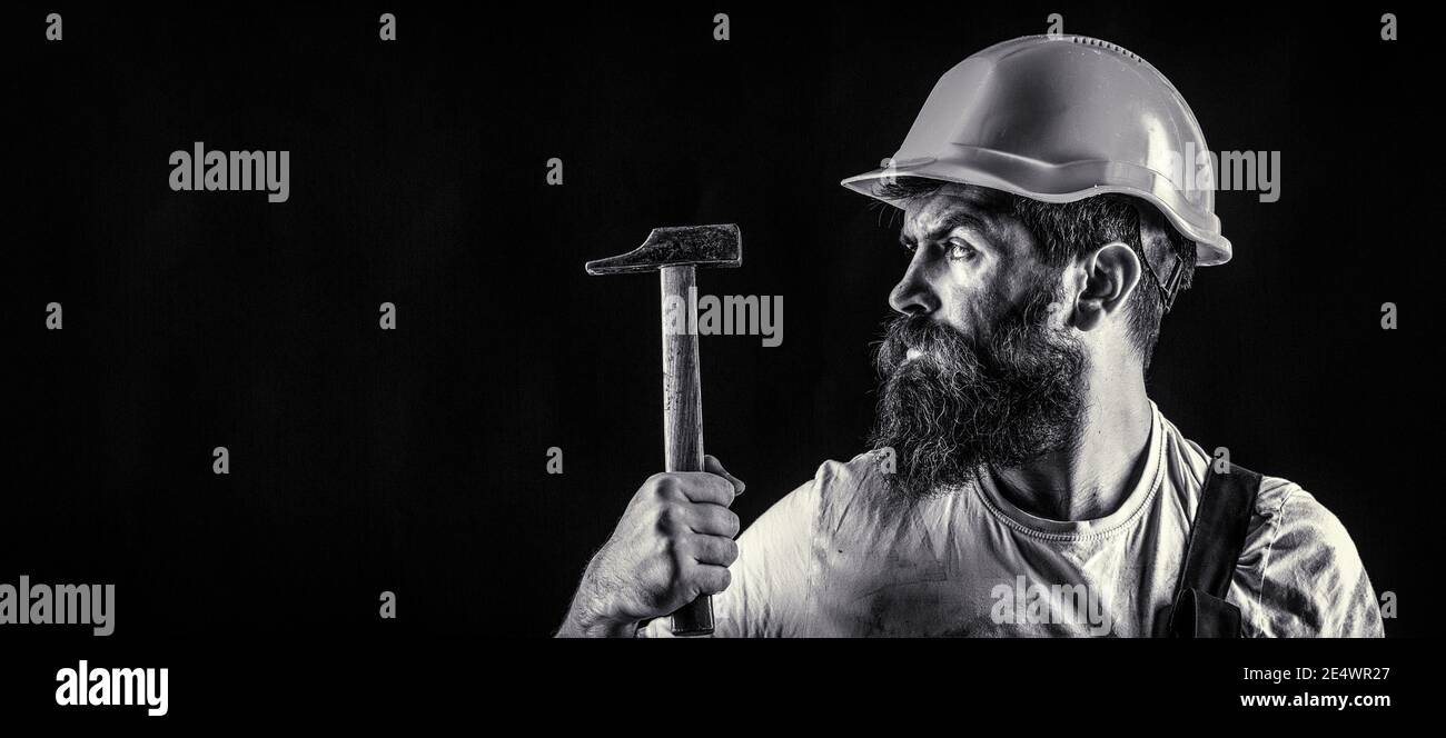 Handyman Services. Industria, tecnologia, uomo costruttore, concetto. Uomo con barba, casco da costruzione, elmetto. Martellatura con martello. Builder in Foto Stock