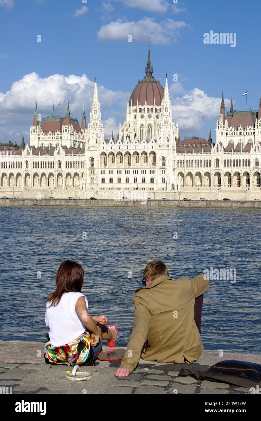 Budapest, Ungheria - 04 aprile 2012: Una giovane coppia siede sul lungofiume del Danubio Blu di fronte al monumentale Parlamento ungherese in Foto Stock