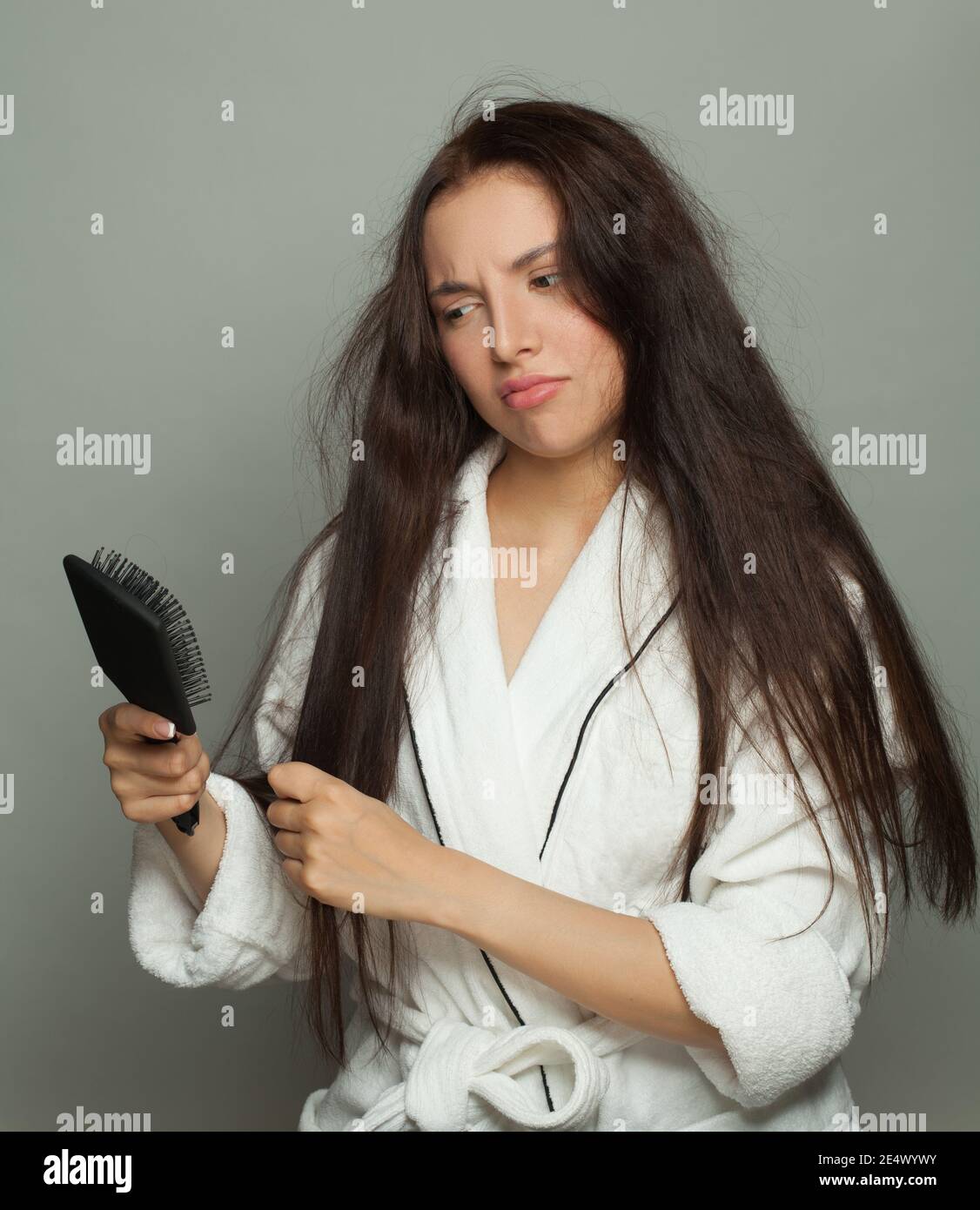 Donna brunetta con capelli aggrovigliati guardando il pettine su sfondo bianco, la cura dei capelli e il concetto di problema dei capelli Foto Stock