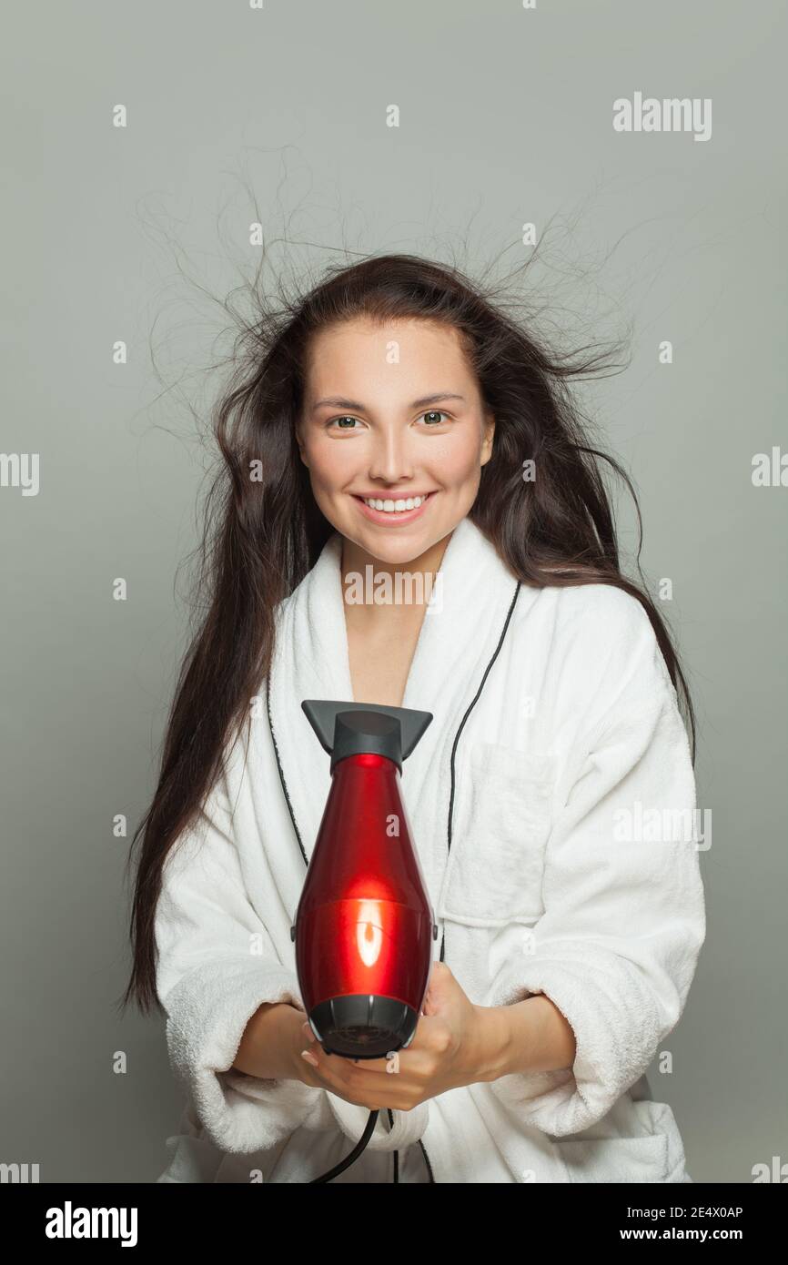 Donna bruna felice che tiene l'asciugacapelli rosso su sfondo bianco Foto Stock