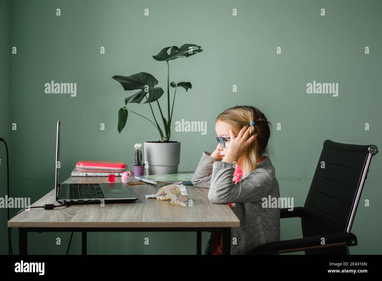 Bambina in occhiali che hanno una lezione online a casa Foto Stock