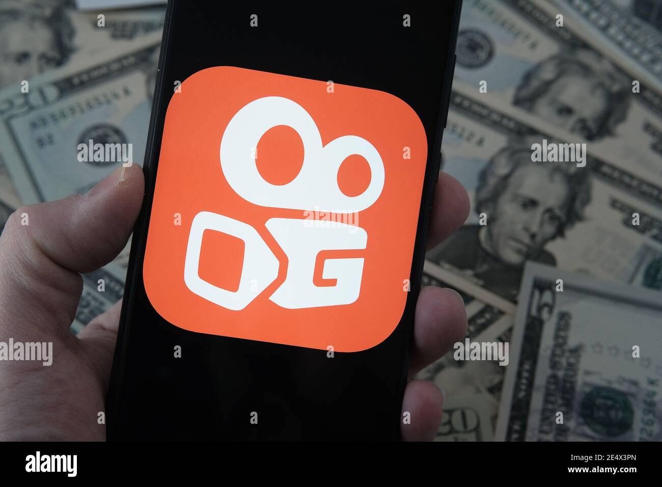 Stafford, Regno Unito - Gennaio 25 2021: Logo dell'app Kuaishou sullo schermo dello smartphone e banconote in dollari sfocate sullo sfondo. Concetto per Foto Stock