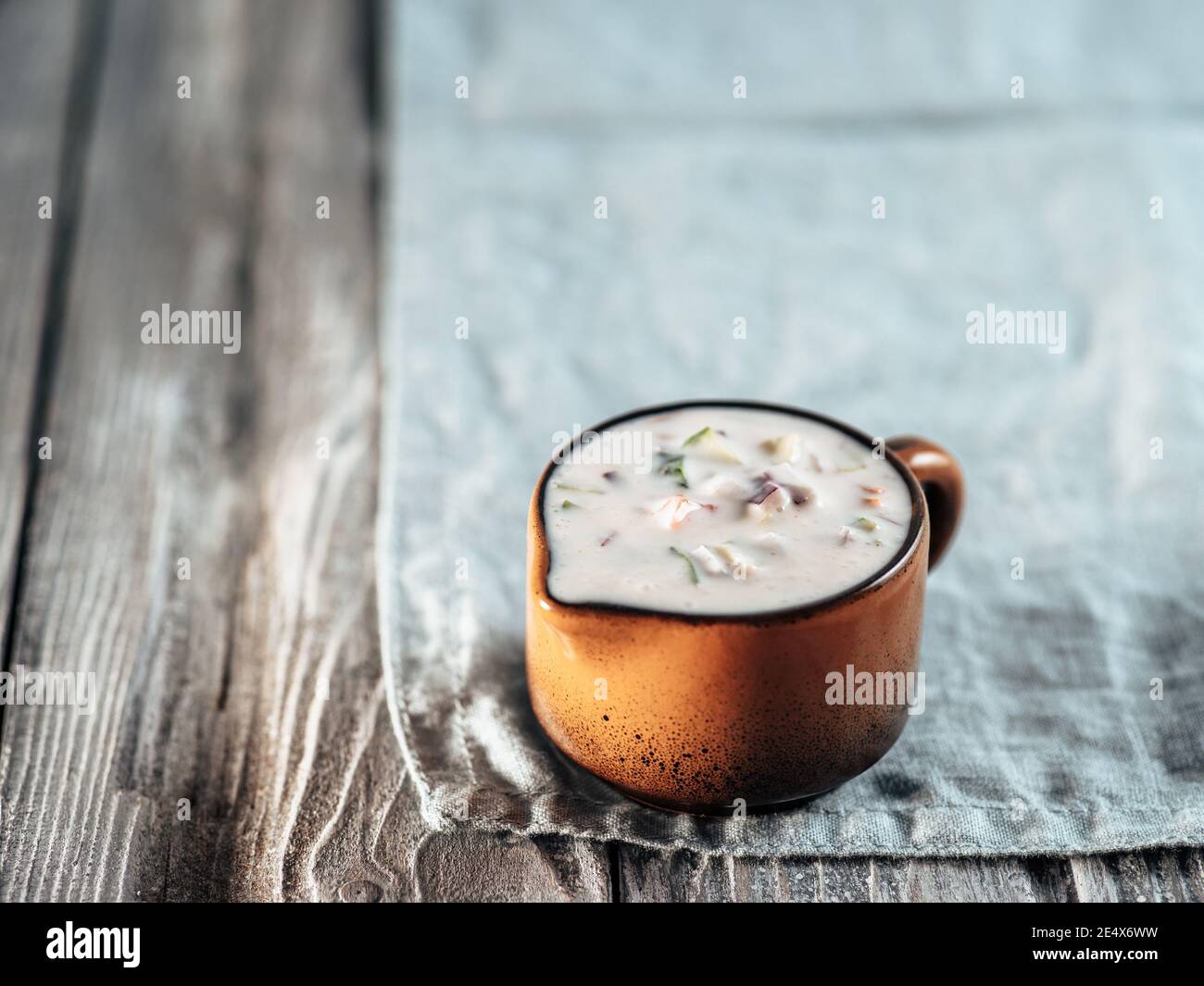 Autentica salsa raita di cetrioli pakistani su tovagliolo di lino blu su sfondo grigio di legno. Salsa di raita immergere con cetrioli, cipolla e pomodoro in trivella di ceramica marrone. Spazio di copia Foto Stock