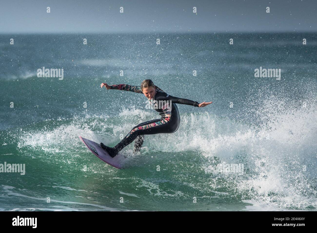 Spettacolare azione di surf come una giovane donna surfer cavalca un wave a Fistral a Newquay in Cornovaglia. Foto Stock