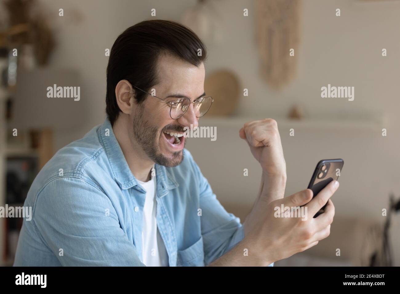 Un ragazzo millenario stupito che legge le notizie perfette dallo schermo del telefono cellulare Foto Stock