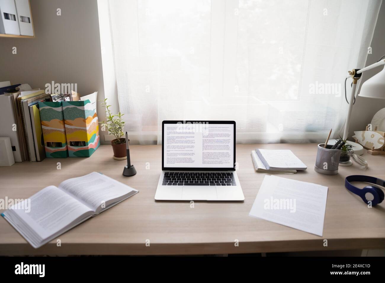 Accogliente ufficio domestico con computer portatile, documenti cartacei e set di cuffie Foto Stock