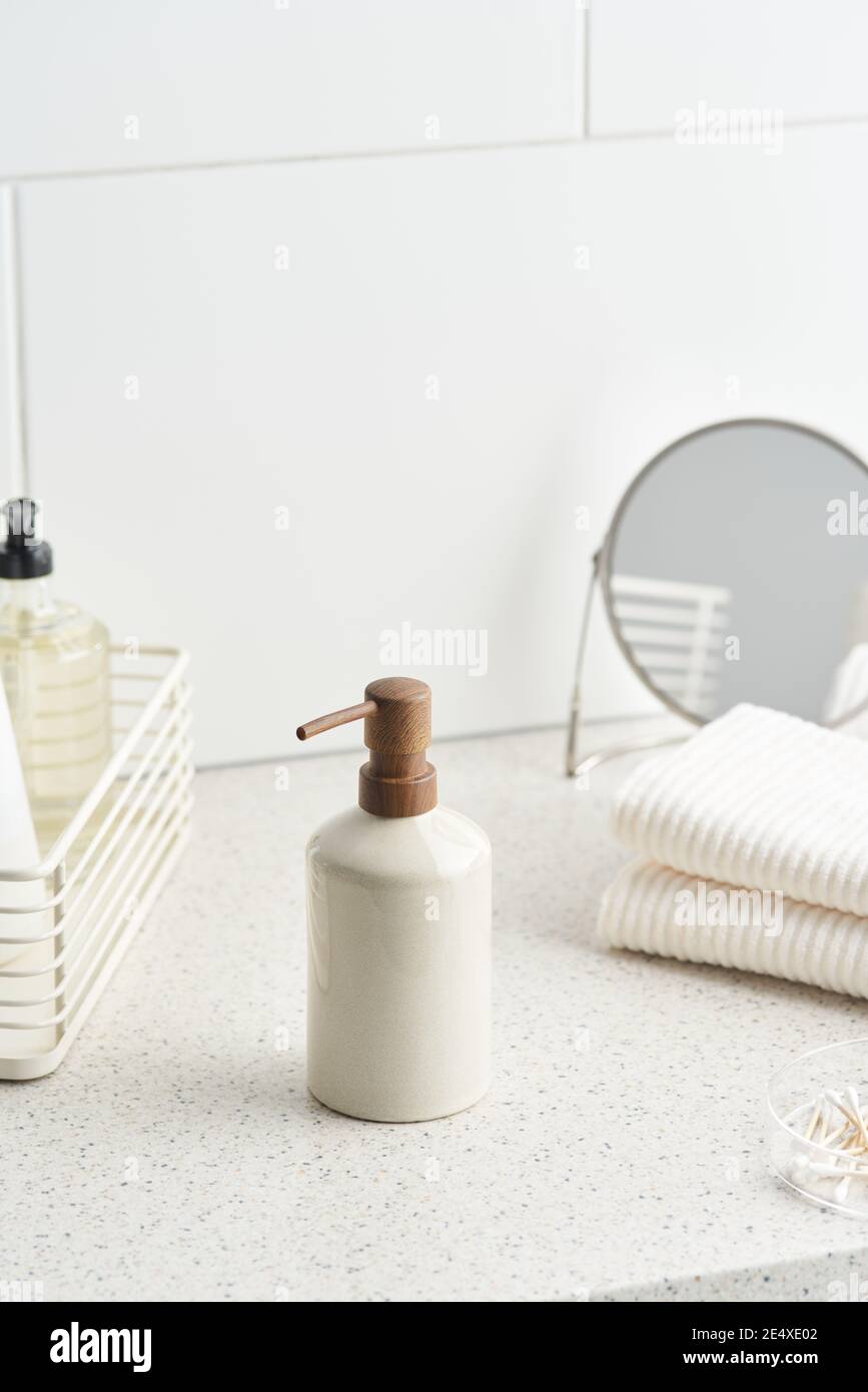 Bottiglia riutilizzabile di sapone organico posta vicino a asciugamani e specchio su ripiano in bagno al mattino Foto Stock