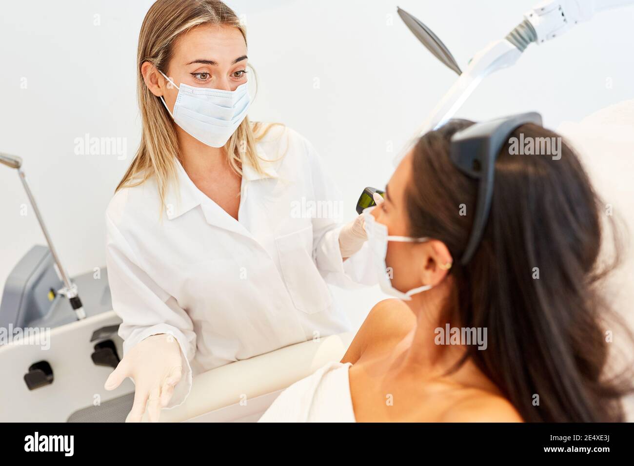 Estetista e paziente con maschera facciale durante l'epilazione laser nello studio cosmetico Foto Stock