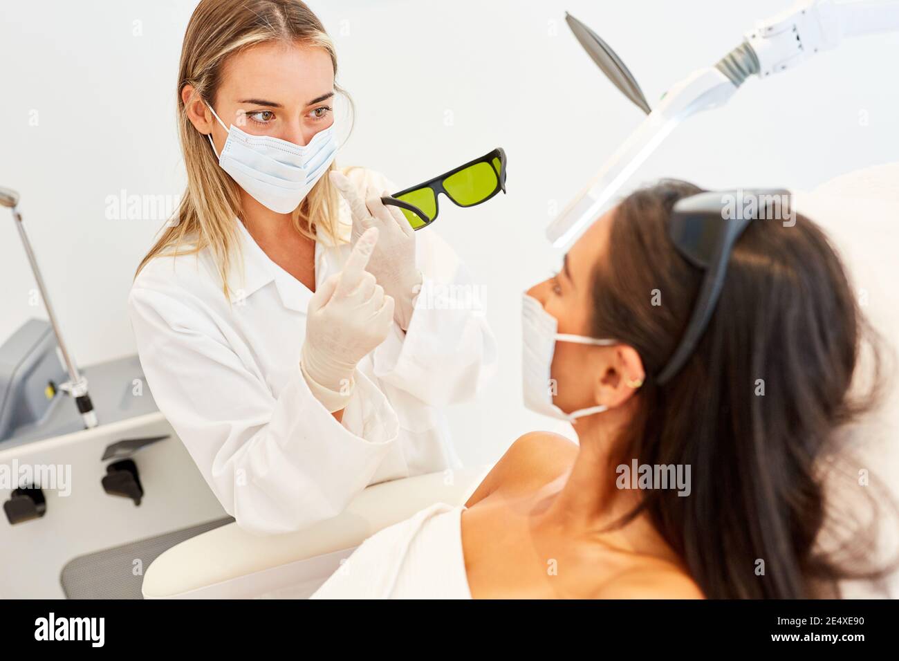 Medico o estetista con maschera mostra gli occhiali protettivi del paziente per terapia laser Foto Stock