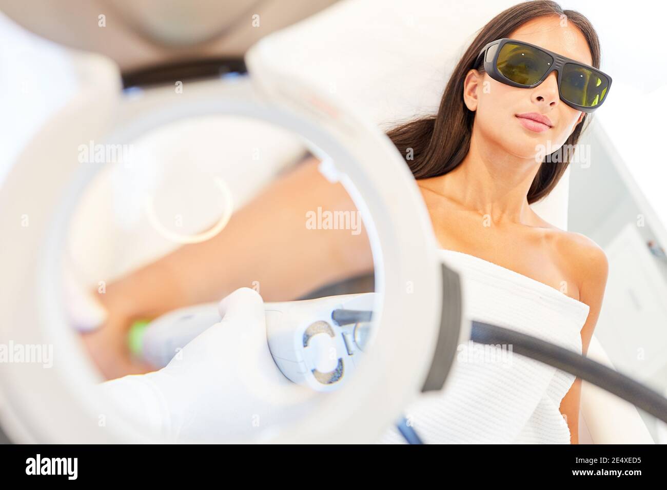 Giovane donna con occhiali protettivi con epilazione laser su di lei braccio sotto la lente di ingrandimento Foto Stock