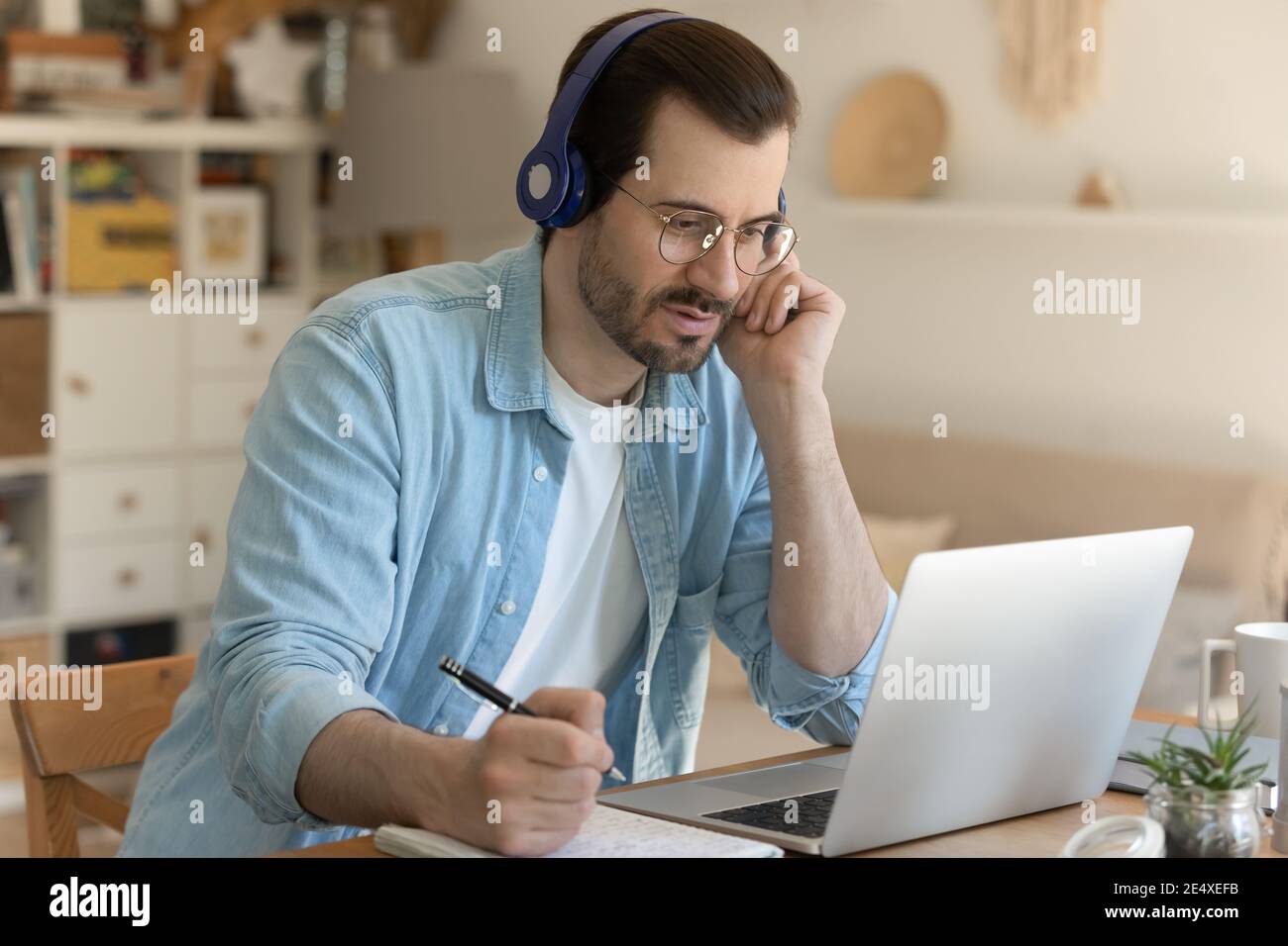 Giovane uomo che ottiene l'istruzione remota seduto da un computer portatile in cuffie Foto Stock