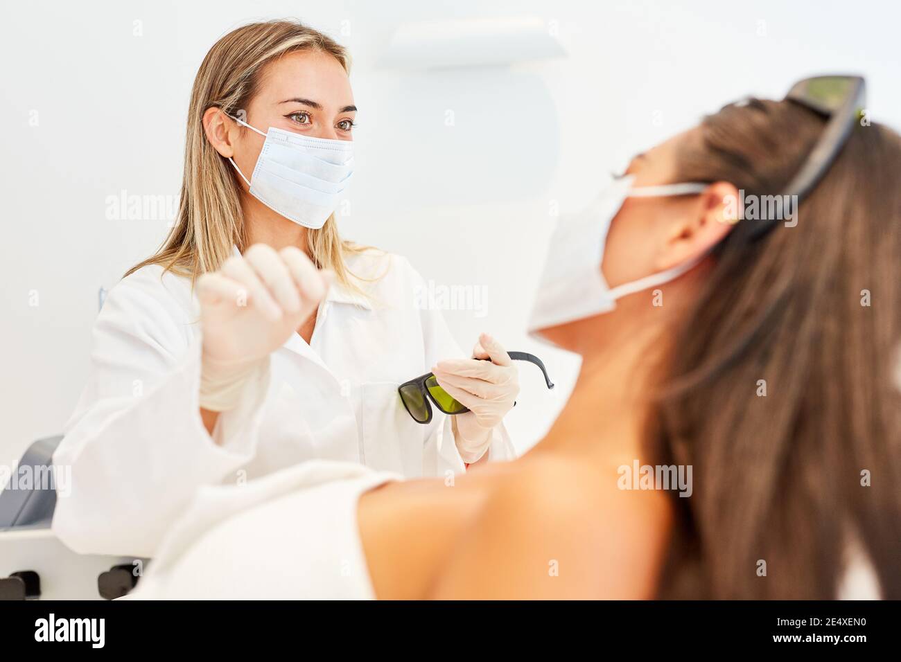 Medico femminile con maschera facciale durante un trattamento per a. giovane donna nella clinica di bellezza Foto Stock