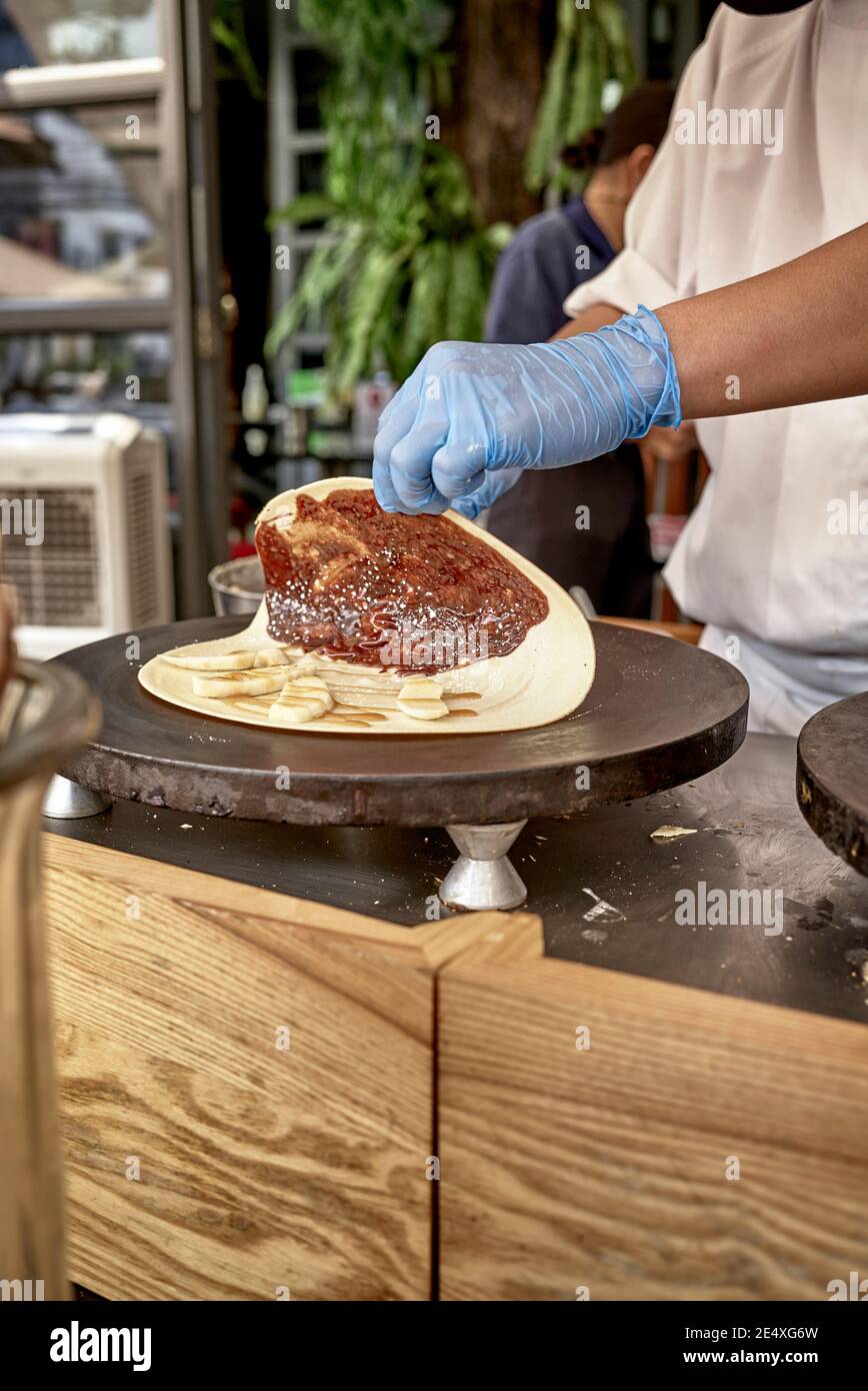 Chef cucina all'aperto al banco del ristorante Covid, con limitazioni per i pasti al coperto e anche fornire un servizio di take-away per crepes preparato sopra una piastra riscaldante Foto Stock