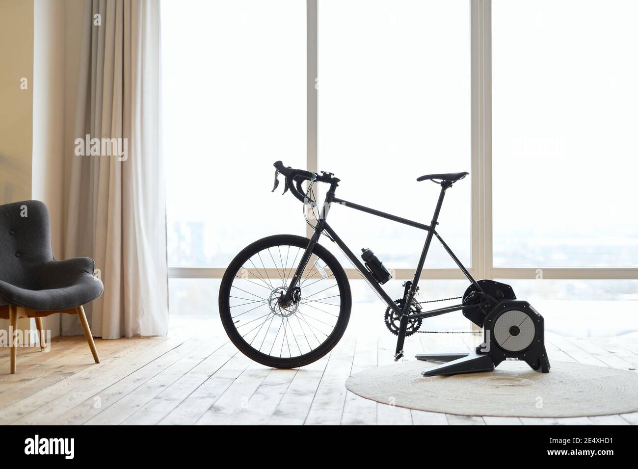 Cyclette nera o allenatore in camera con grande finestre e sedia Foto Stock