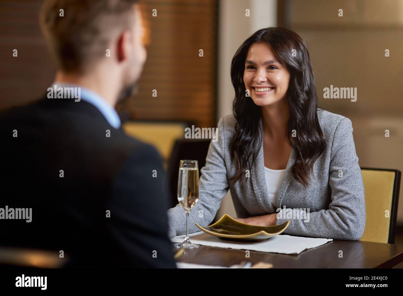 Donna luminosa bruna sorridente mentre guarda il suo compagno seduto attraverso di lei al tavolo del ristorante Foto Stock