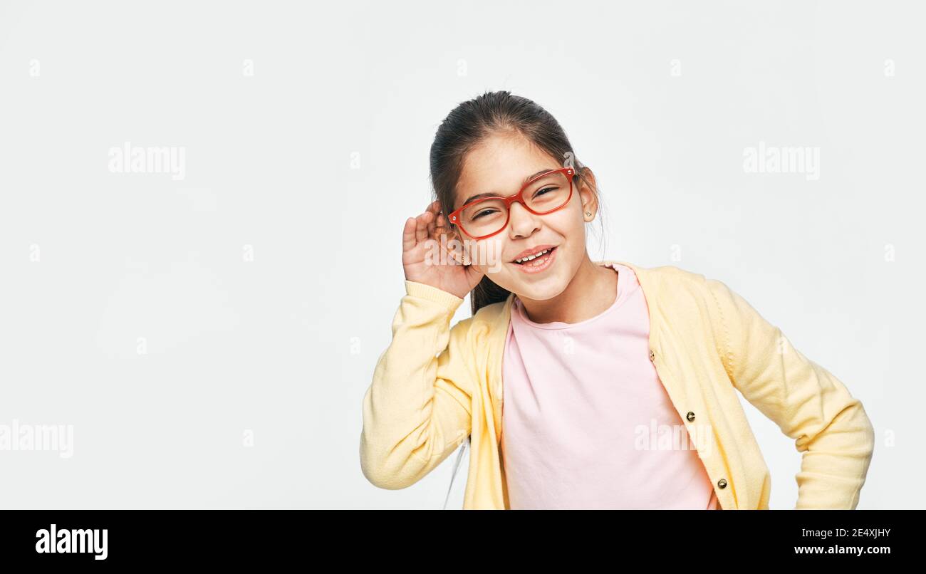 Concetto di sordità infantile. Carina ragazza mista razza con una mano sopra l'orecchio ascoltando suoni e voci, isolato su grigio Foto Stock