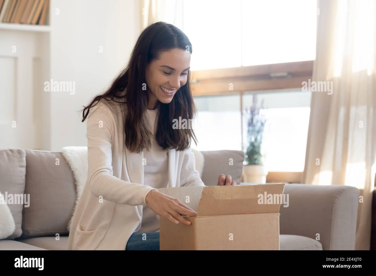 Una donna curiosa che si è aperta con una confezione di cartone e un pacco a casa Foto Stock