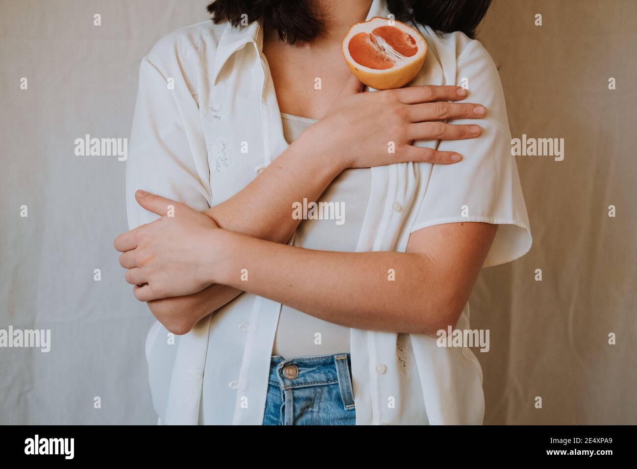 Colpo di closeup di una donna in una blusa bianca che tiene un taglio arancione sulla spalla Foto Stock