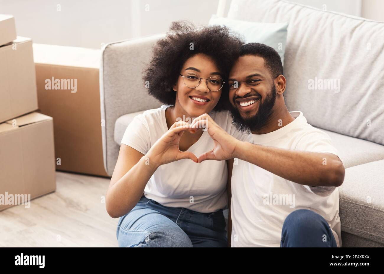 Coppia africana seduta tra le scatole in movimento gesturing forma del cuore all'interno Foto Stock