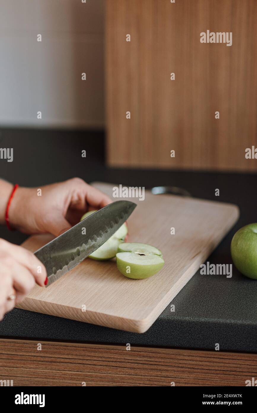 Colpo verticale di una donna che taglia la mela su una tavola in cucina Foto Stock