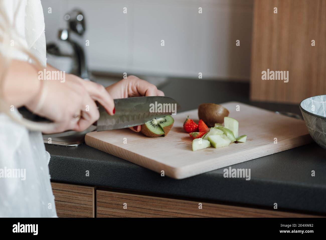 Primo piano di una donna che taglia frutta fresca su un asse in cucina Foto Stock