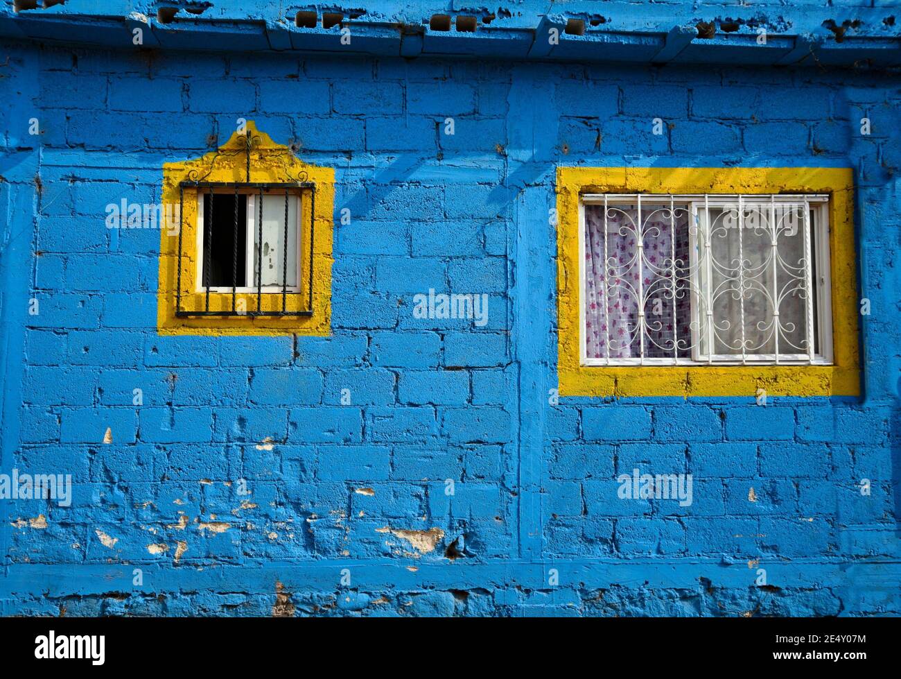 Vecchia facciata tradizionale casa con una parete di blocchi di Malta blu, finestre con rifiniture gialle e griglie di ferro artigianali in Atlixco, Puebla Messico. Foto Stock