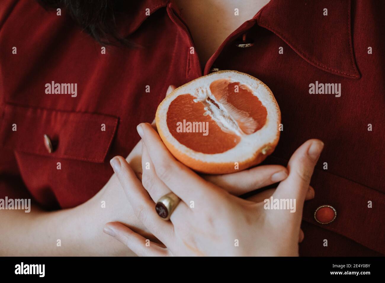 Closeup di una donna che tiene un arancio tagliato su di lei torace Foto Stock