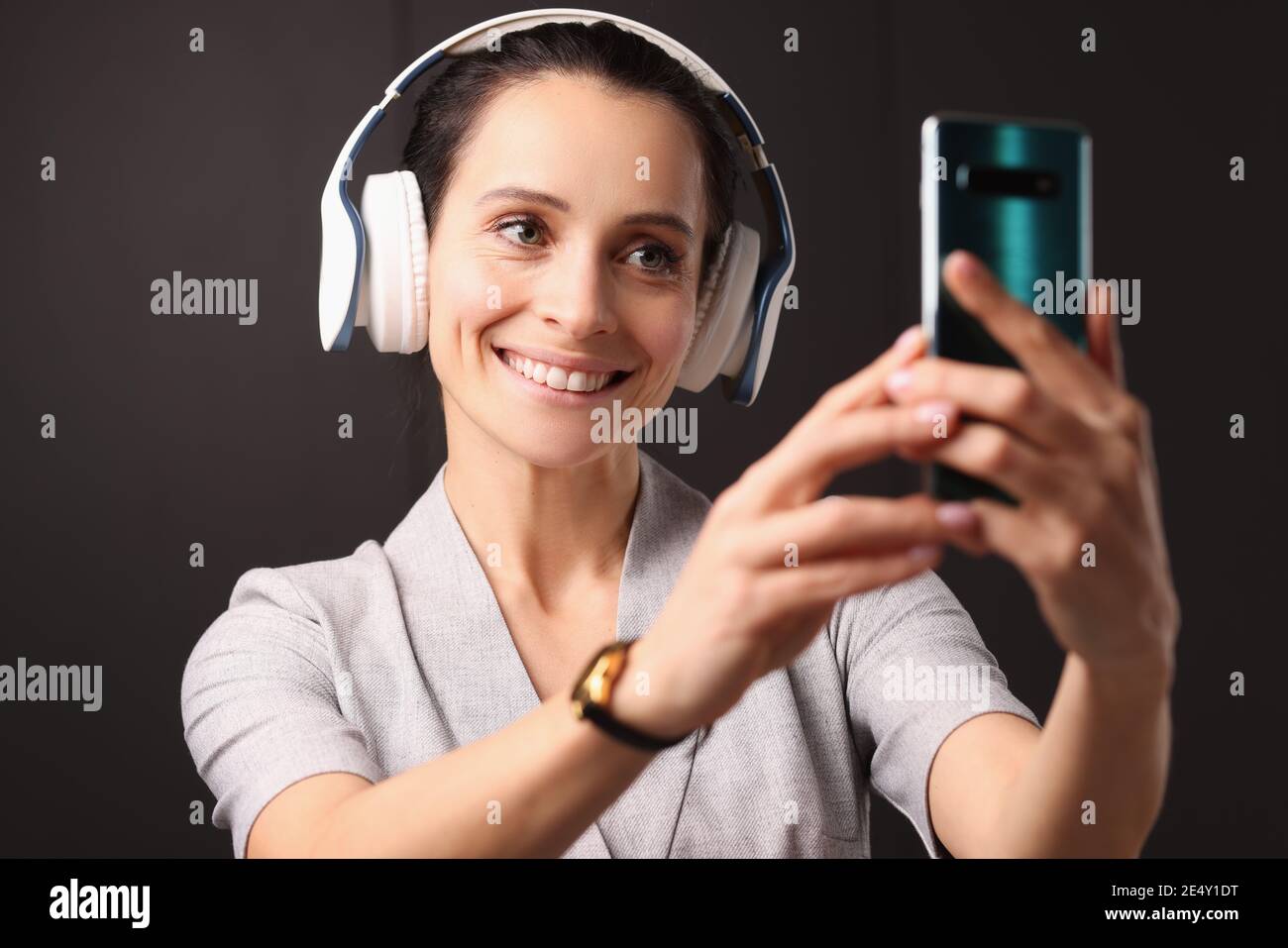 Una donna sorridente con le cuffie guarda allo smartphone Foto Stock