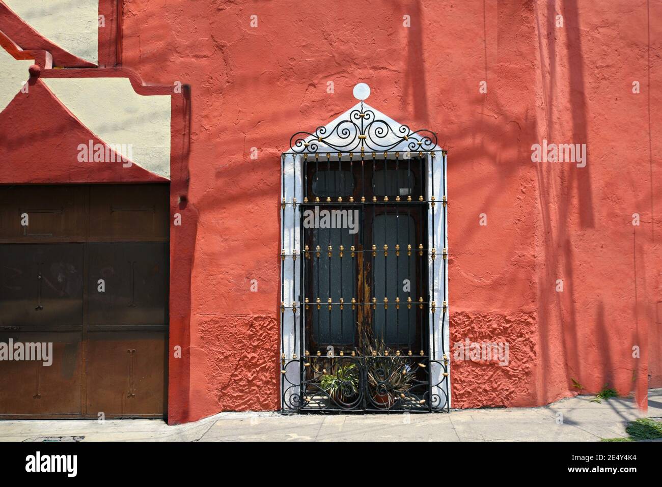 Vecchia facciata coloniale con una parete in stucco rosso veneziano e una finestra con finiture bianche e griglie in ferro artigianali ad Atlixco, Puebla Messico. Foto Stock