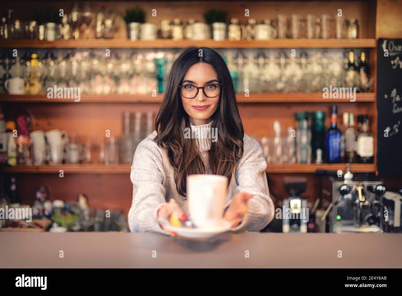 Un colpo di cameriera sorridente in piedi dietro il bancone e tenendo una tazza di tè in mano. Foto Stock