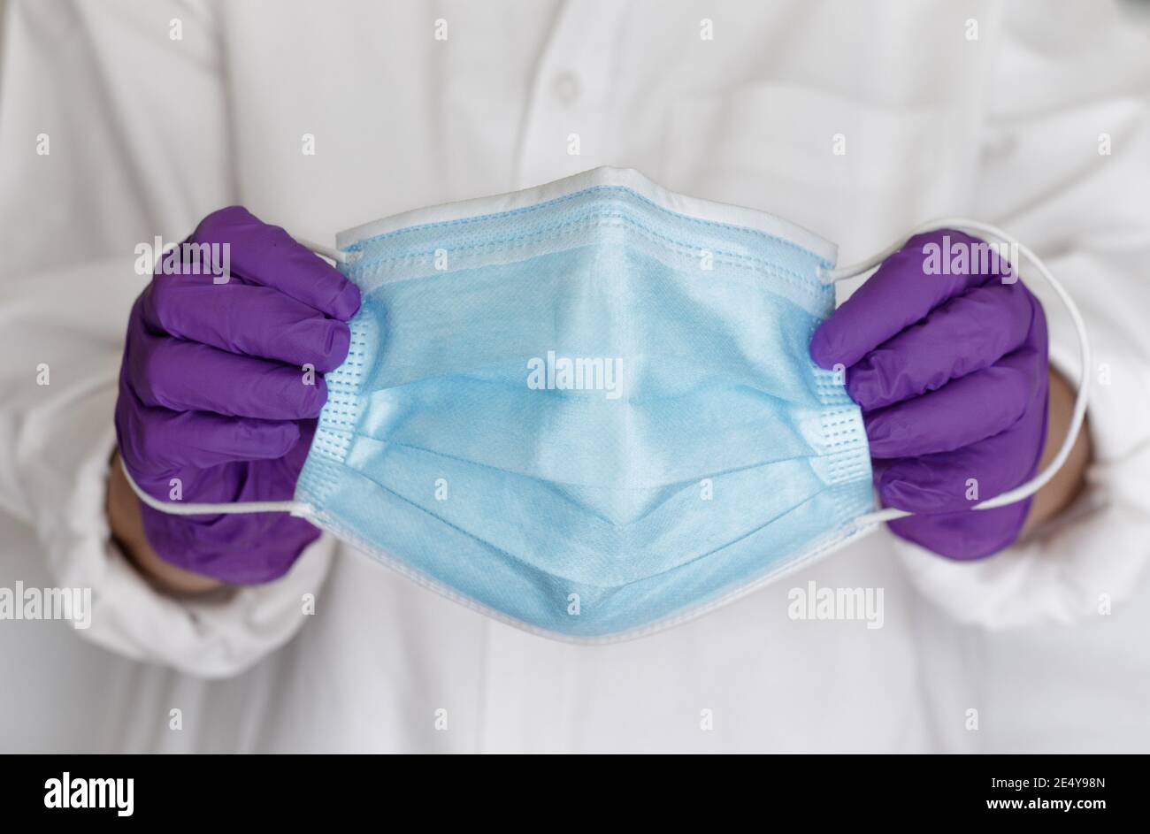 Maschera chirurgica tenuta da un medico con guanti. Maschera medica protettiva blu per fermare la diffusione di virus e germi Foto Stock