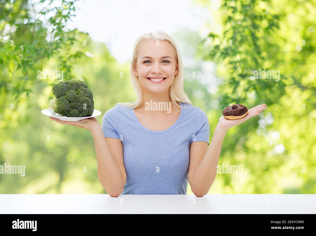 Donna sorridente scegliendo tra i broccoli e ciambella Foto Stock