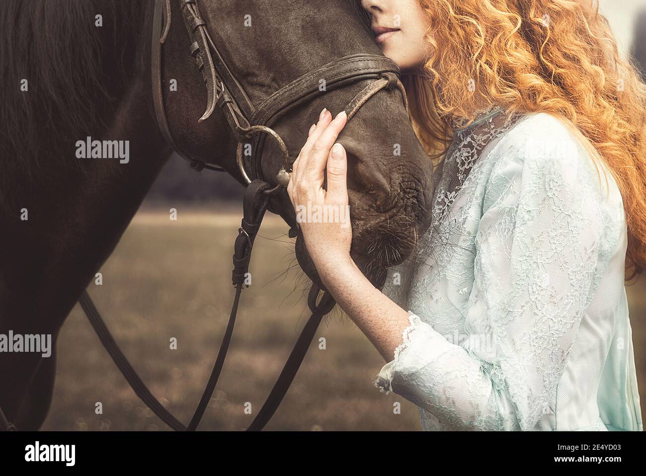 Amore per gli animali. Giovane Donna senza volto vestita in un elegante abito d'epoca, dolcemente coccolando un cavallo, stropicchiando la testa. Foto Stock