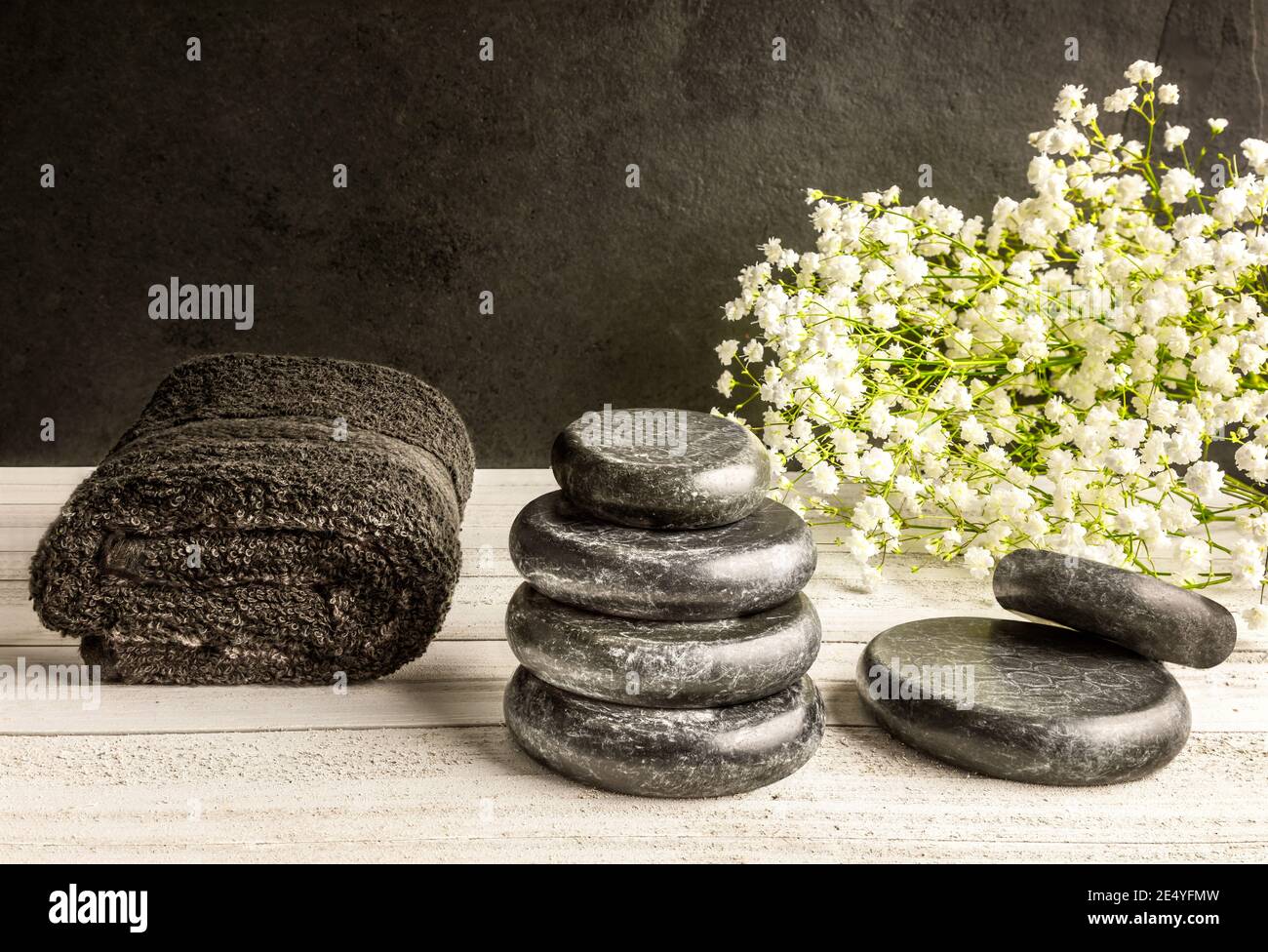 Massaggio pietre basaltiche per il centro termale e un asciugamano e fiori bianchi foglie o sfondo scuro. Foto Stock