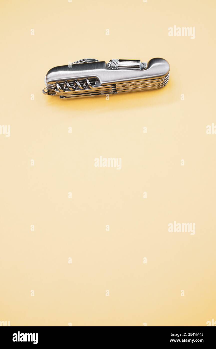 Immagine verticale di un piccolo coltello tascabile pieghevole su un superficie beige sotto le luci Foto Stock