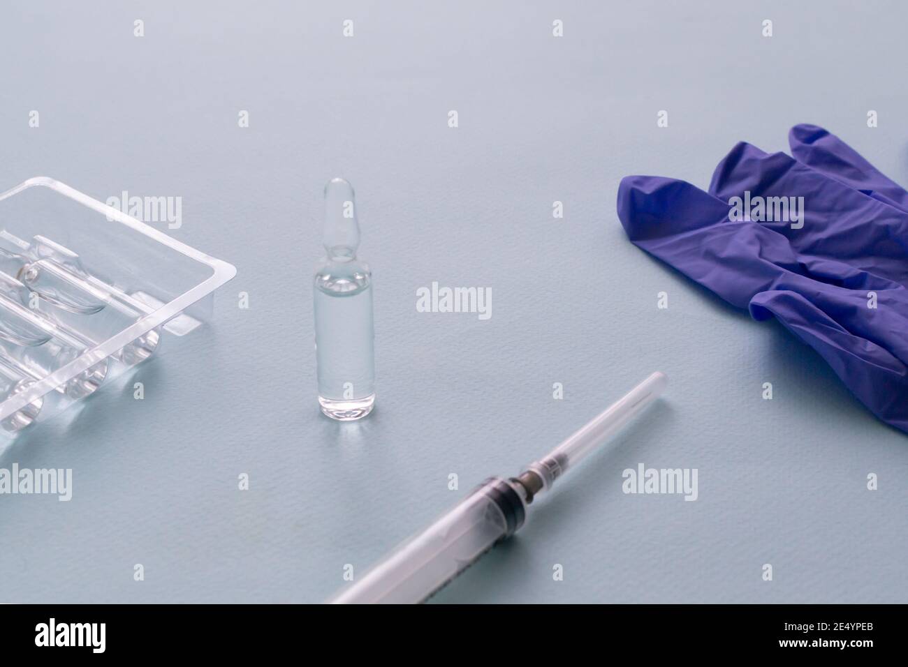 Vaccino e siringa con guanti medici su sfondo blu. Vaccinazione. COVID-19, SARS - concetto di vaccino CoV2. Spazio di copia. Foto Stock