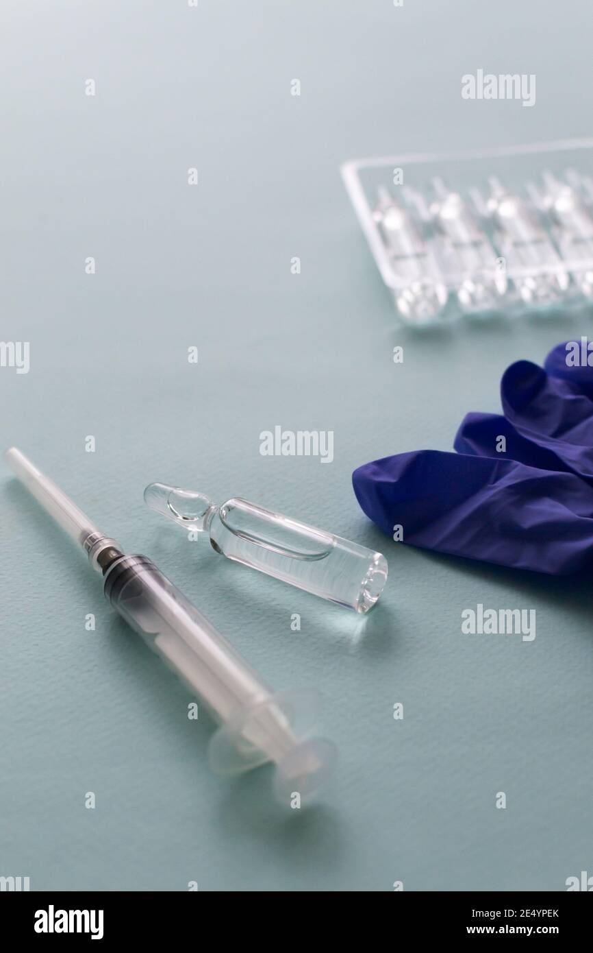 Vaccino e siringa con guanti medici su sfondo blu. Vaccinazione. COVID-19, SARS - concetto di vaccino CoV2. Spazio di copia. Orientamento verticale. Foto Stock