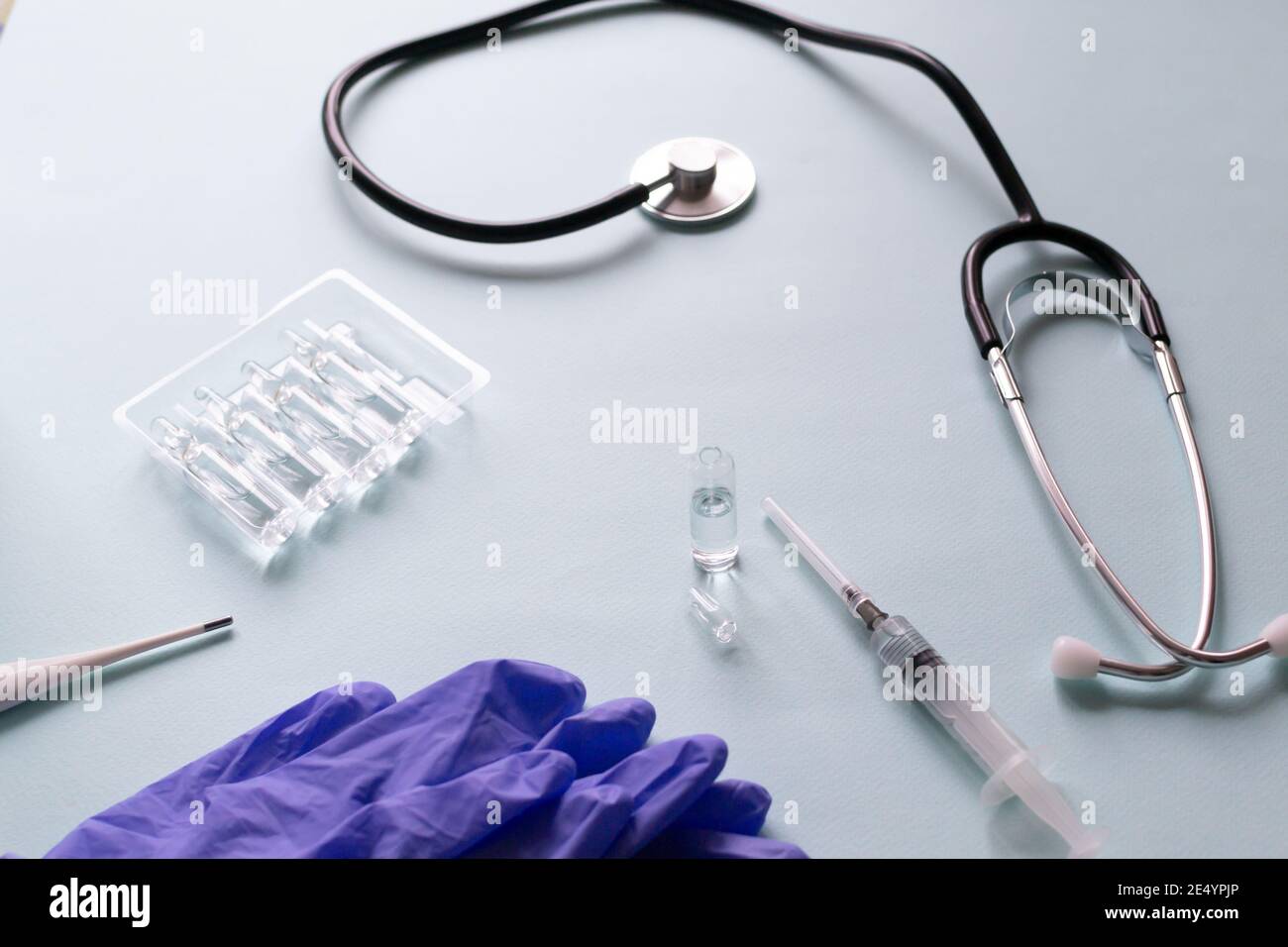 Vaccino circondato da dispositivi medici su sfondo blu. Vaccinazione. COVID-19, SARS - concetto di vaccino CoV2. Spazio di copia. Orientamento orizzontale. Foto Stock