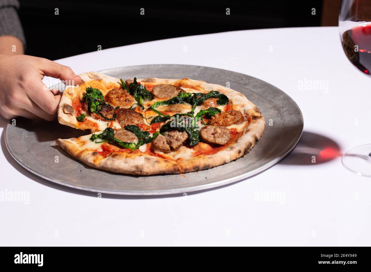 Mano che afferra la fetta di Brick forno Pizza con salsiccia e. Broccoli Raab Foto Stock
