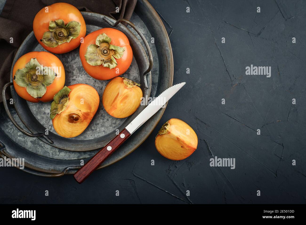 Frutta fresca Persimmons biologica matura su vassoio metallico con fetta su sfondo nero, vista dall'alto Foto Stock
