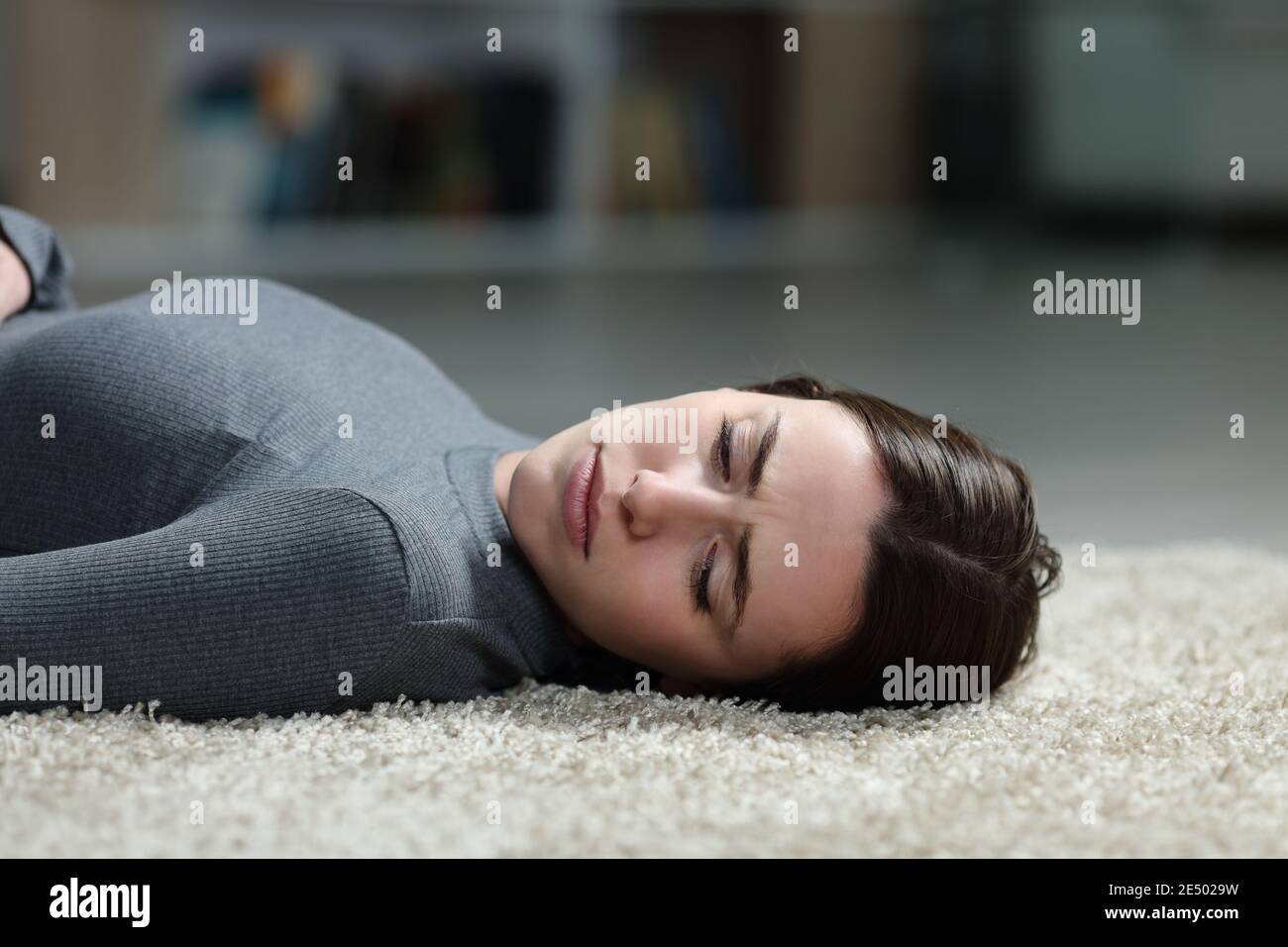 Donna triste che guarda via sdraiata su un tappeto sul piano di casa Foto Stock