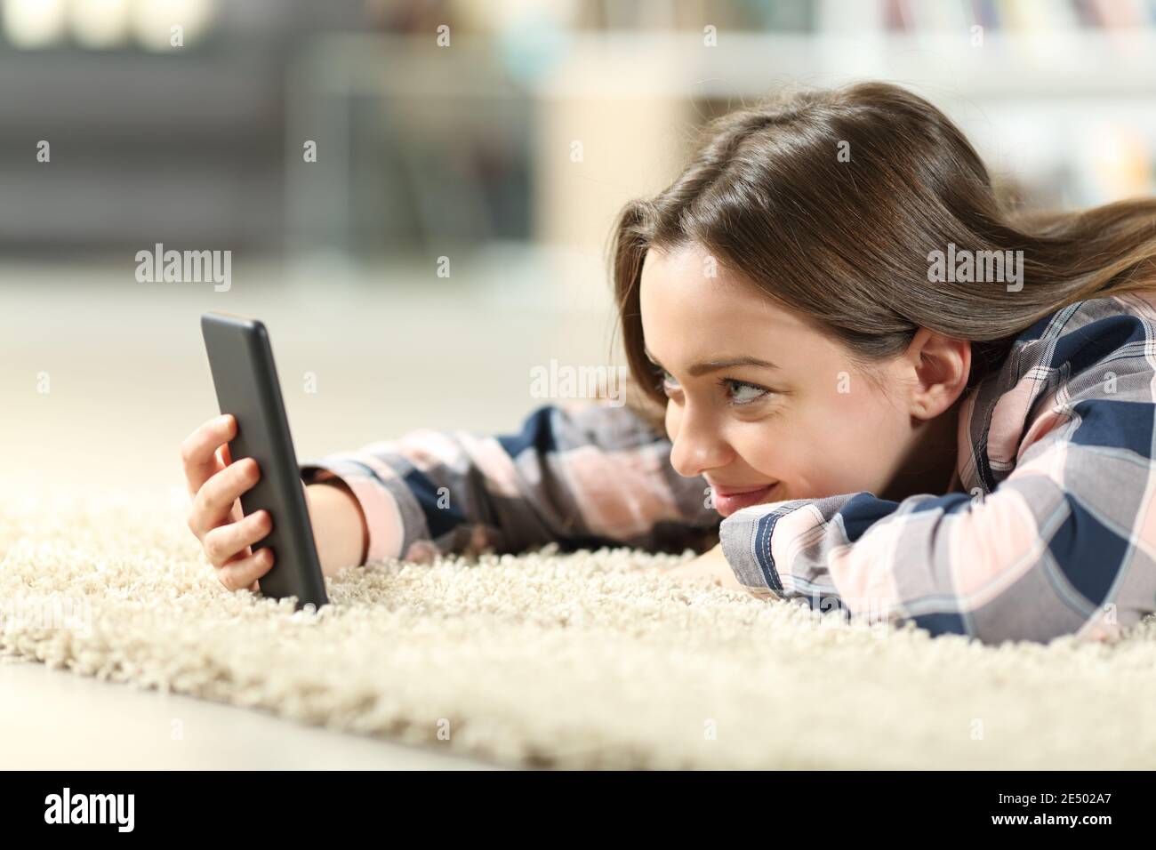 Felice teen che controlla il contenuto dello smartphone che si trova su un tappeto nel soggiorno di casa Foto Stock