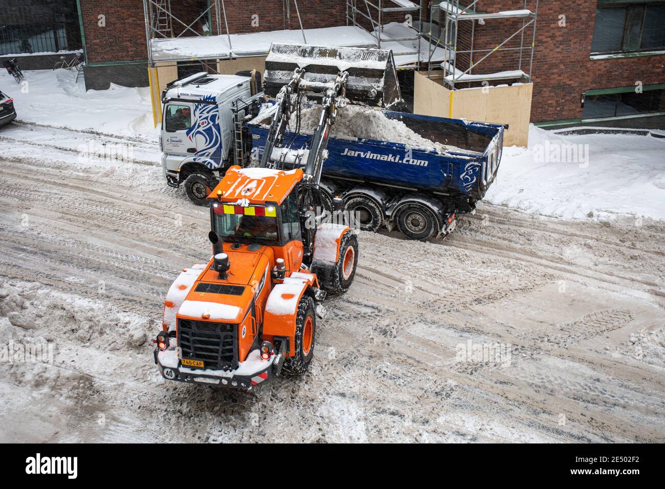 Caricatore che sradia le rive di neve in un dumper a Messeniuksenkatu nel distretto di Taka-Töölö di Helsinki, Finlandia Foto Stock
